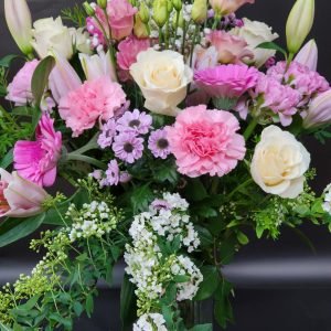 An elegant arrangement in a vase featuring a harmonious blend of pastel shades, showcasing the delicate beauty of roses, carnations, and lilies, accented with lush green foliage. A symphony of soft hues and natural textures, capturing the essence of timeless floral elegance."