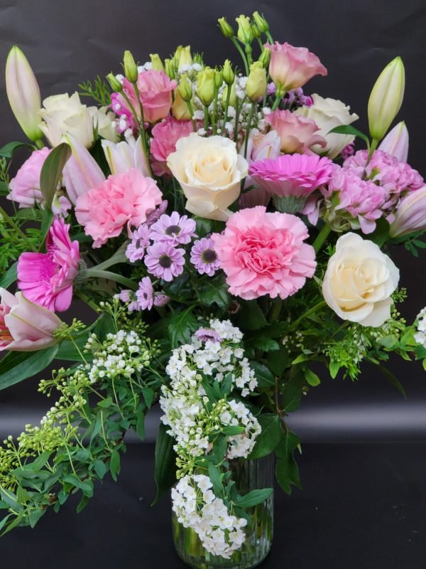 An elegant arrangement in a vase featuring a harmonious blend of pastel shades, showcasing the delicate beauty of roses, carnations, and lilies, accented with lush green foliage. A symphony of soft hues and natural textures, capturing the essence of timeless floral elegance."